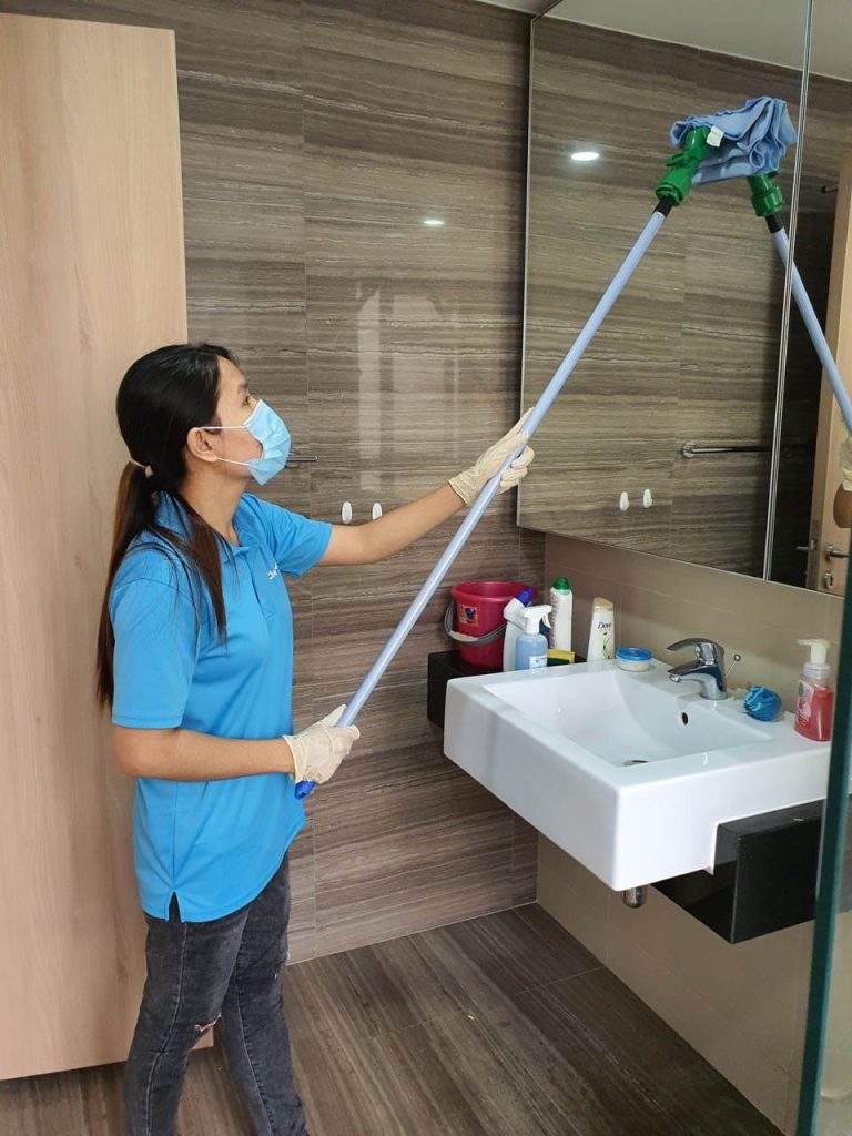 A professional cleaner in Seattle wearing a mask and gloves wipes bathroom mirror with an extendable tool — using certified organic products to protect families, kids, and pets
