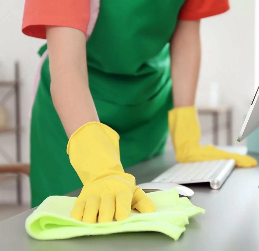 Professional cleaner in green apron and yellow gloves sanitizing office desk with eco-friendly microfiber cloth — pet-safe, non-toxic disinfectant for businesses in Austin.