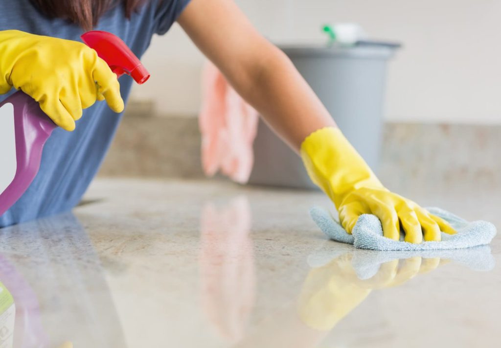 Professional cleaner in yellow gloves wiping down marble floor with disinfectant spray — deep cleaning service for homes and apartments in Austin, Denver & Seattle