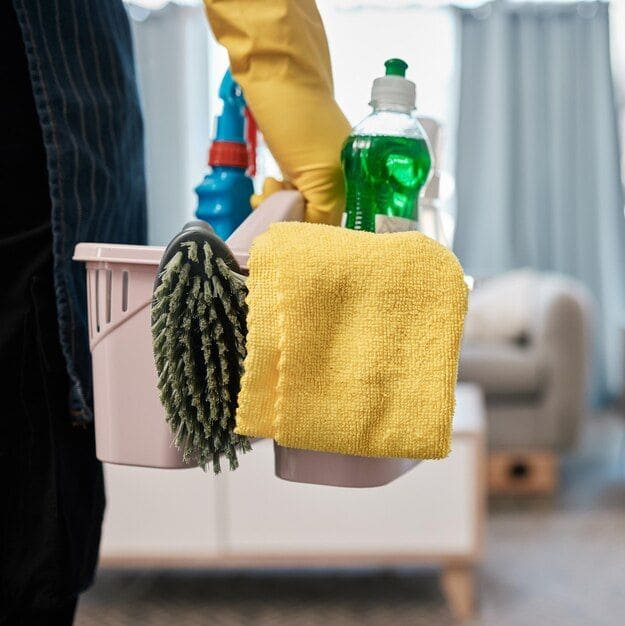 Cleaning caddy with eco-friendly supplies — microfiber cloth, green disinfectant, and scrub brush for apartment cleaning in Austin