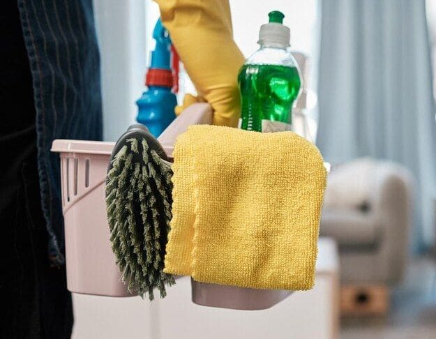 Professional cleaner’s supply caddy in Austin: yellow microfiber cloth, green eco-friendly dish soap, blue disinfectant spray, and dusting mitt—ready for deep home or apartment cleaning with pet-safe, non-toxic products.