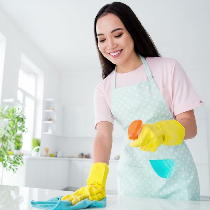 Smiling professional cleaner spraying disinfectant on kitchen counter in bright Austin apartment — eco-friendly, baby-safe cleaning services