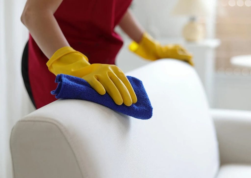 Professional apartment cleaning in Austin: certified cleaner dusting white sofa with eco-friendly microfiber cloth — pet-safe, non-toxic, and baby-safe home cleaning service by Gleaming Space
