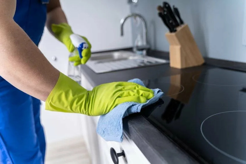 Professional cleaner in blue uniform using eco-friendly disinfectant and microfiber cloth for same-day kitchen cleaning in Austin — pet-safe, baby-safe, spotless results