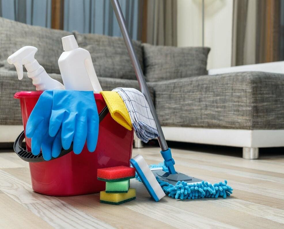 Red bucket with eco-friendly cleaning supplies—gloves, microfiber cloths, spray bottles, and a mop—ready for professional apartment or house cleaning in Round Rock. Certified organic products ensure a safe, thorough clean.
