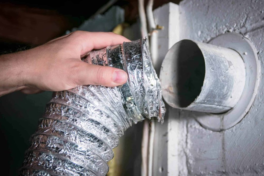 Close-up of HVAC technician securing flexible air duct to supply vent register with professional tools and equipment
