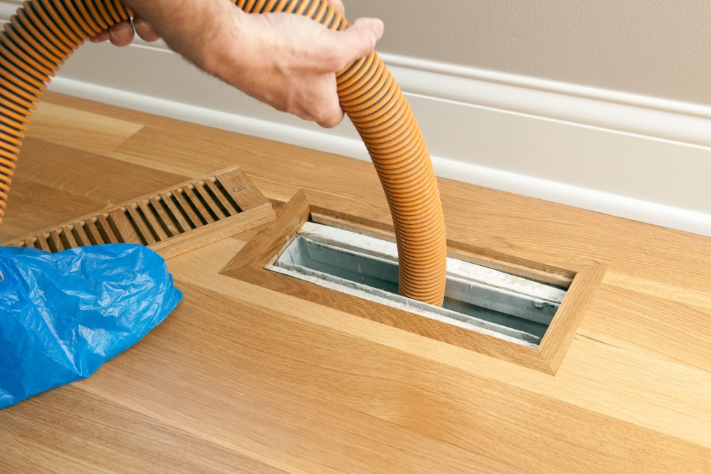 Expert duct cleaning specialist using high-powered suction on floor register during comprehensive residential air duct cleaning and HVAC maintenance
