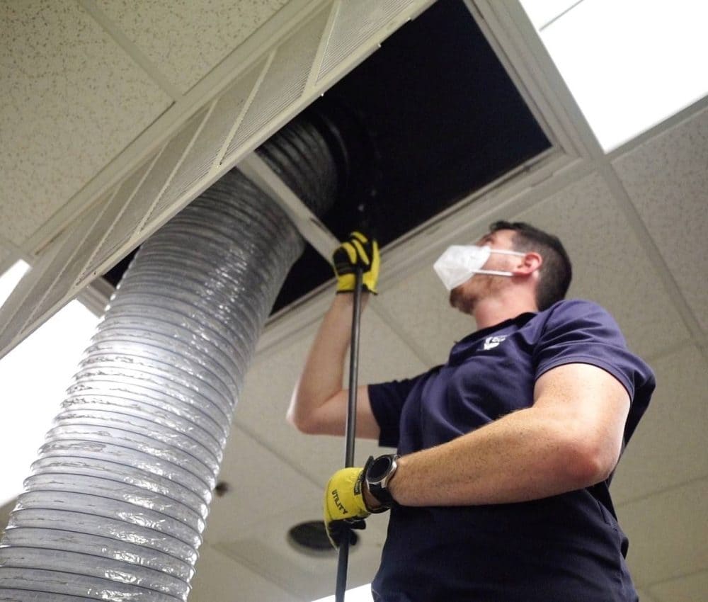 Certified technician performing professional air duct cleaning with protective equipment in Austin TX
