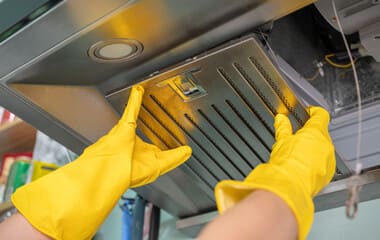 Professional kitchen hood and exhaust cleaning in Denver - certified technician wearing protective gloves removing grease buildup from commercial kitchen ventilation system filters and ductwork
