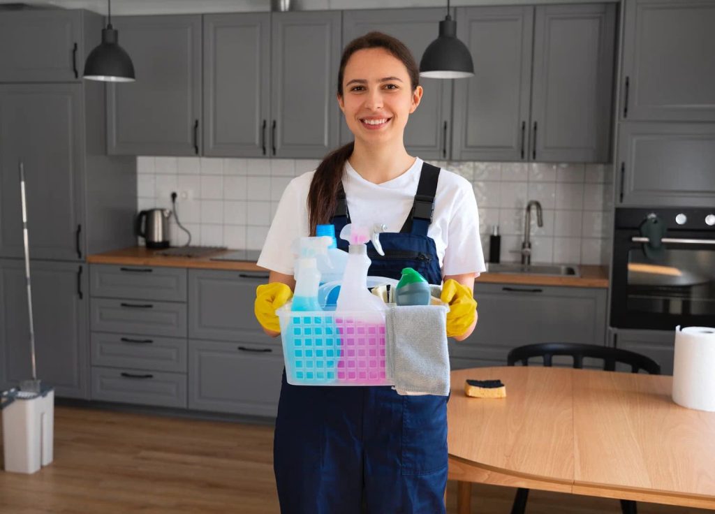 Trusted professional cleaner in Englewood smiles while holding a caddy of organic cleaning products — ready to deliver a full home cleaning service with eco-friendly, non-toxic solutions for Denver-area families.