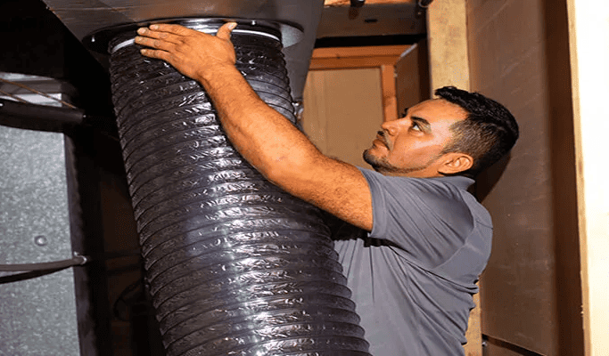 A Gleaming Space technician connects a truck-mounted HEPA vacuum hose to an HVAC air handler during commercial or residential duct cleaning