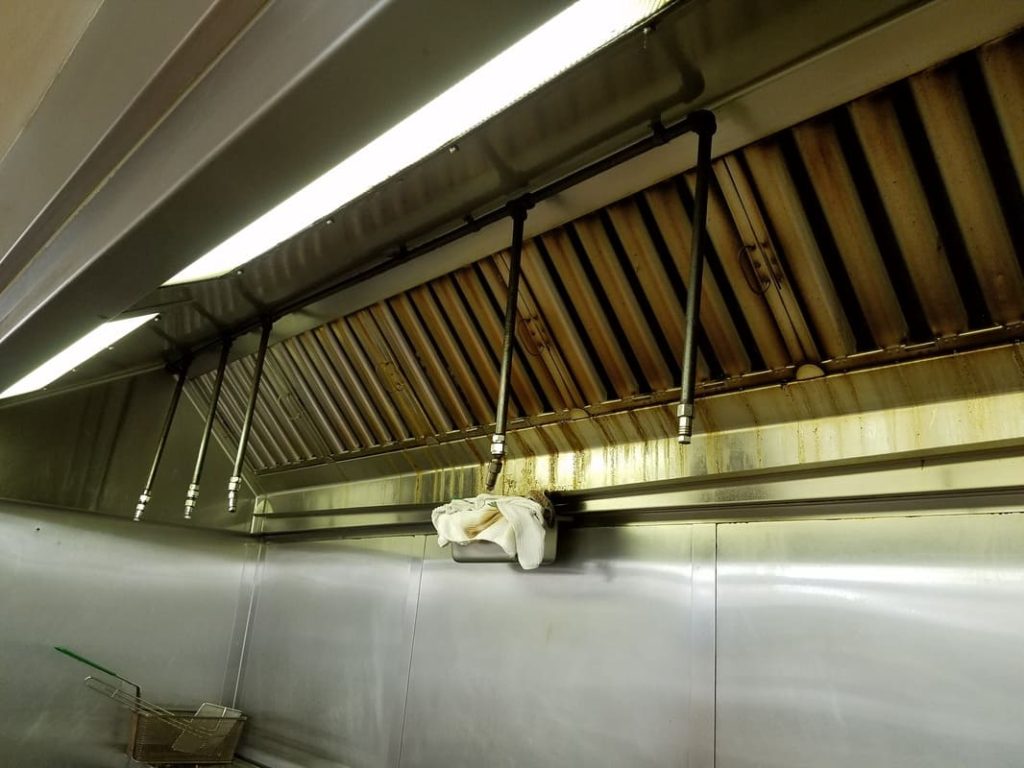 Commercial kitchen exhaust hood with baffle filters showing grease accumulation before professional cleaning service