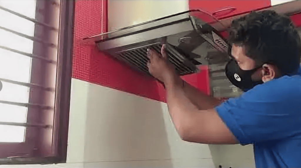 Professional technician cleaning kitchen range hood ventilation system with protective mask and blue uniform