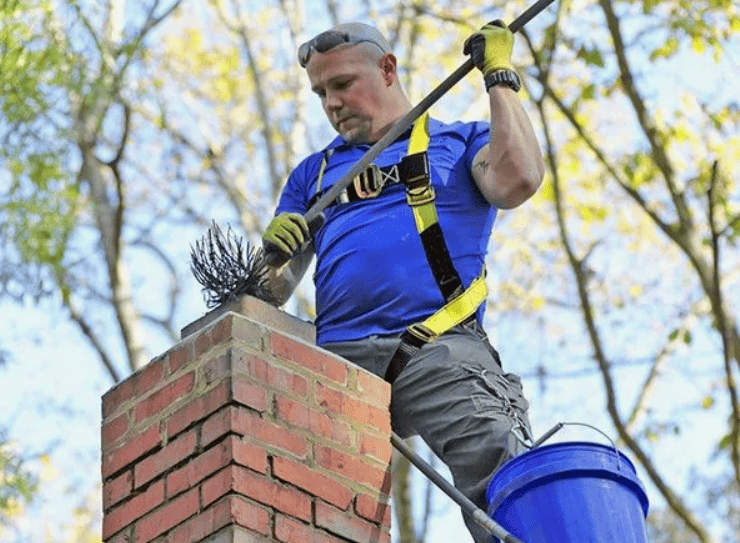 Professional chimney sweep technician cleaning brick chimney with specialized brush and safety equipment